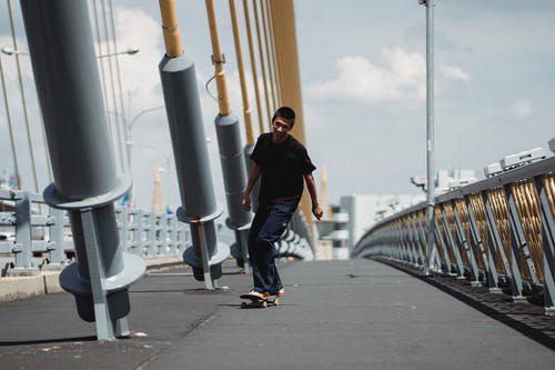 亚洲男子骑滑板在桥上 · 免费素材图片
