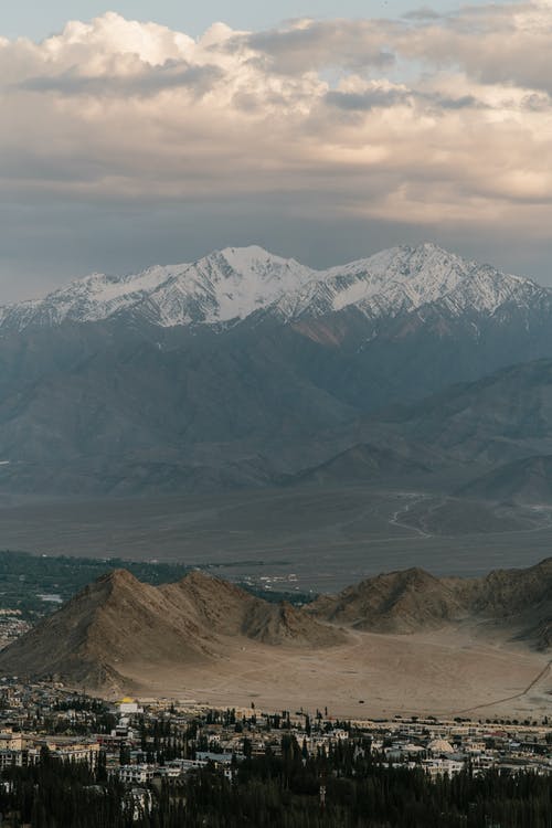 多云的天空下小镇附近的高雪山 · 免费素材图片