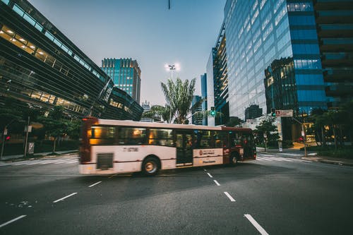 白天，高层建筑附近道路上的白色巴士 · 免费素材图片