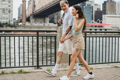 时尚多样的夫妇手牵着手，漫步在河桥下的城市长廊 · 免费素材图片