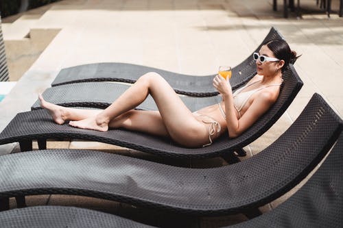年轻苗条的女人躺在日光浴浴床和享受刷新饮料 · 免费素材图片