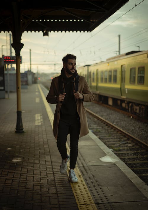 穿棕色外套的男人走在火车站附近 · 免费素材图片