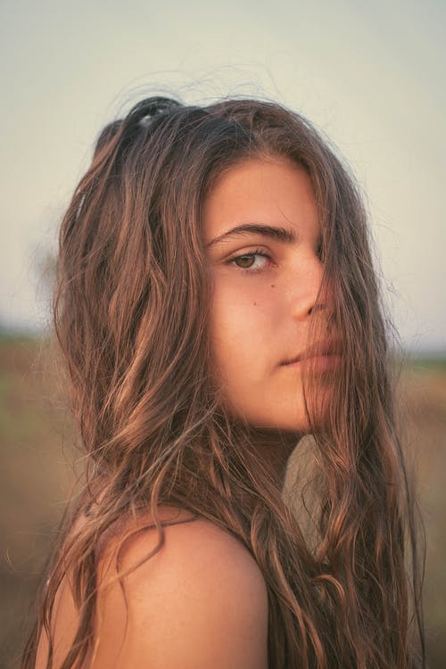 美丽的女人，留着长头发站在模糊的领域 · 免费素材图片