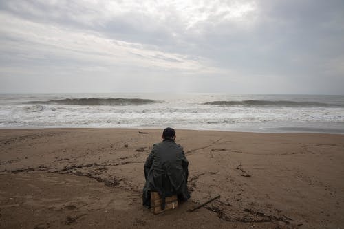 穿着灰色正装衬衫坐在海边的人 · 免费素材图片