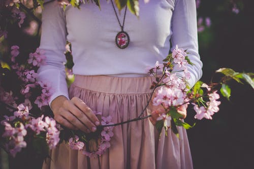 女人穿着白色的长袖衬衫和米色的裙子，拿着粉红色的花瓣花 · 免费素材图片