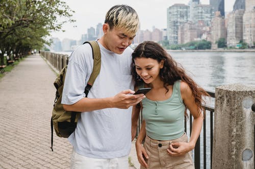在河岸上使用智能手机的满足多种族年轻夫妇 · 免费素材图片