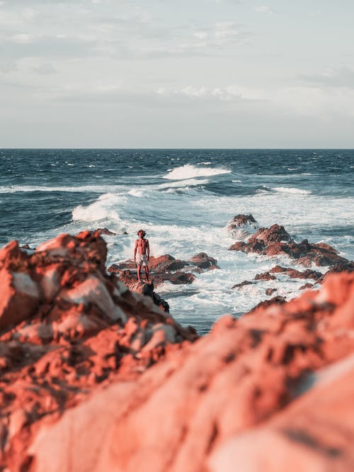 男子站在海边岩层上的摄影 · 免费素材图片