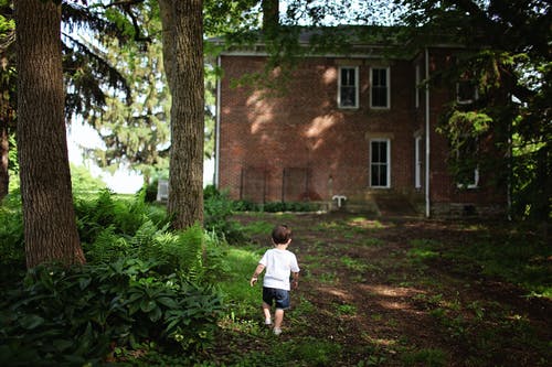 男孩穿着白色圆领t恤和蓝色牛仔短裤走向棕色混凝土建筑 · 免费素材图片