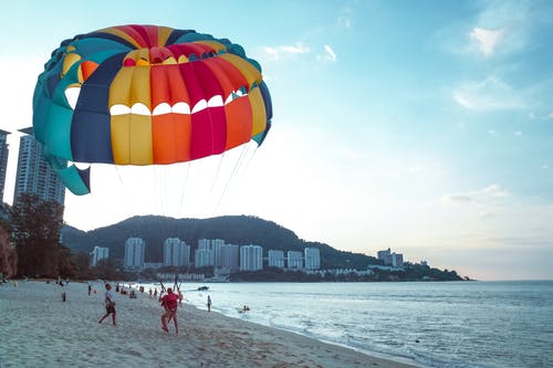 男子在海滩上骑降落伞 · 免费素材图片