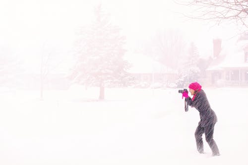 白天在狂暴的雪下举行黑色单反相机的粉红色盖头的女人 · 免费素材图片