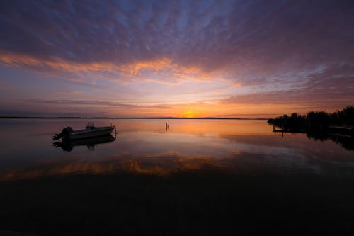 日落时分在平静的水面上的船的轮廓 · 免费素材图片