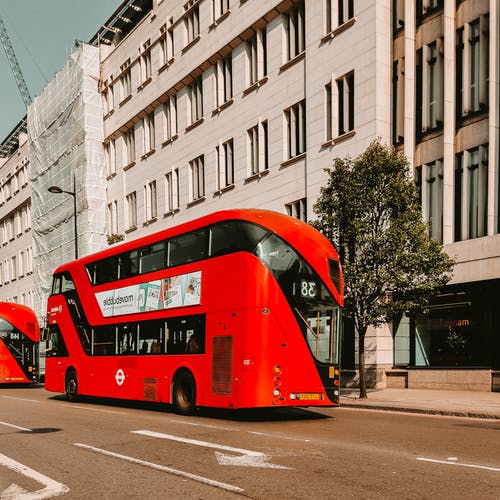 红色双层巴士经过城市的街道 · 免费素材图片