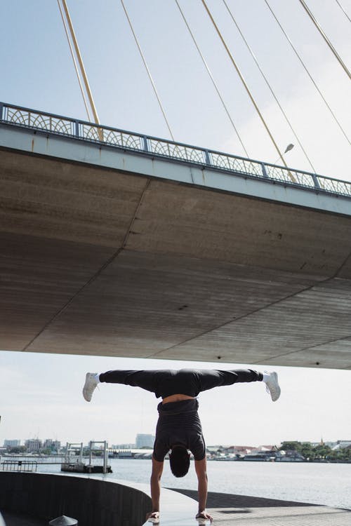 运动员在桥下的路堤上表演倒立 · 免费素材图片