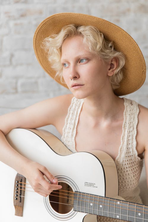 弹吉他的时髦的沉思小姐对白色砖墙 · 免费素材图片