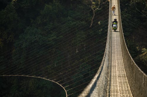 两人骑踏板车，另一个人在桥上行走 · 免费素材图片