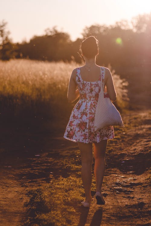 白色和粉红色的花无袖连衣裙在阳光下在布朗路上行走的女人 · 免费素材图片
