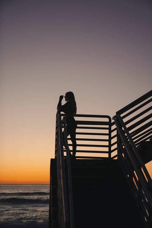 一个女人在日落时站在木码头上的剪影 · 免费素材图片