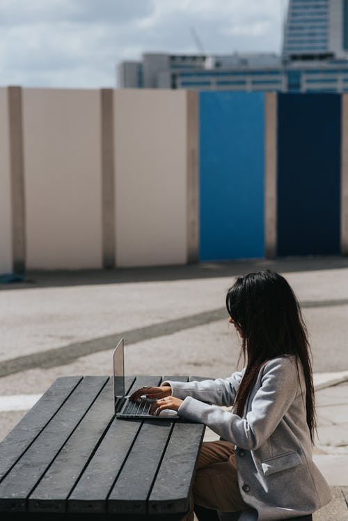 在街头桌上的笔记本电脑上打字的认不出来的族裔女商人 · 免费素材图片