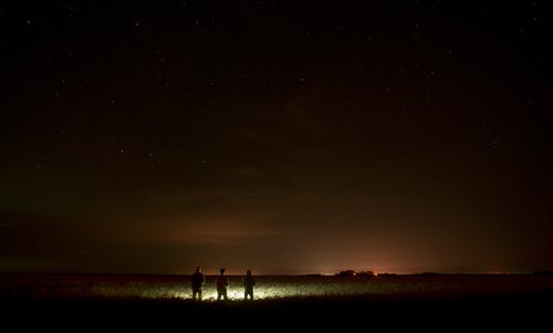 三人在夜间站在沙滩上的灯前 · 免费素材图片