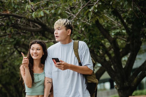 亚洲男朋友附近幸福的族裔女人与智能手机在公园 · 免费素材图片