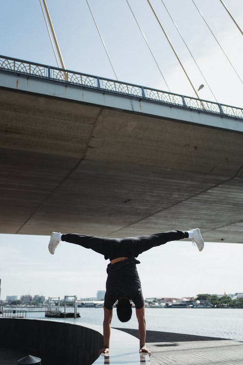 站立在桥梁下的手上的无法认出的灵活的运动员 · 免费素材图片