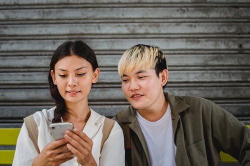 性格开朗的亚洲夫妇，在街头的长椅上浏览智能手机 · 免费素材图片