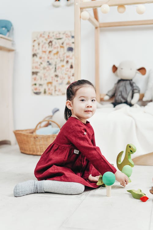 红色长袖连衣裙坐在白色的地上玩玩具的女孩 · 免费素材图片