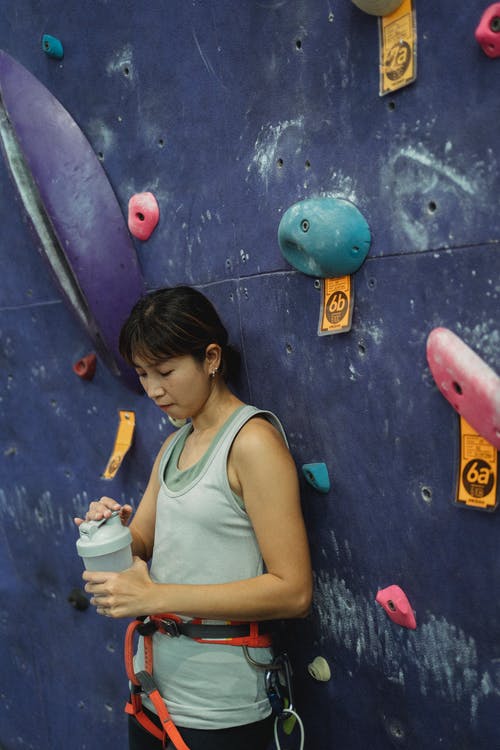 站立与水瓶的亚裔女性登山人在攀登墙壁附近 · 免费素材图片