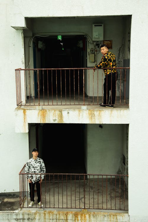 穿着时髦的衣服的年轻亚洲男性站立在生锈的阳台上 · 免费素材图片