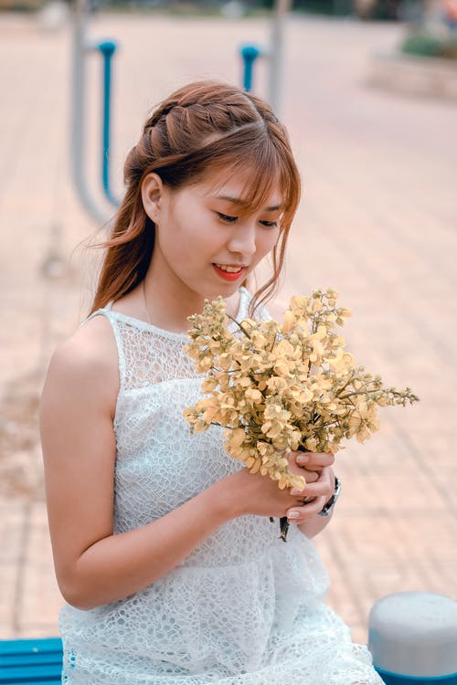 女人穿着白色蕾丝连衣裙，拿着黄色的花花束 · 免费素材图片