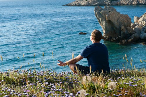 男子坐在花田面对大海 · 免费素材图片