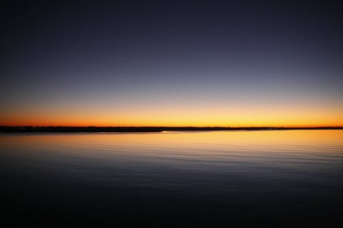 在日落期间蓝色和橙色晴朗的天空下平静的海面剪影 · 免费素材图片