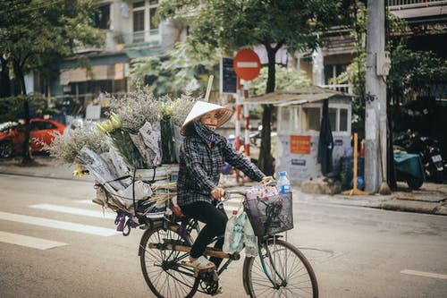 女人骑着自行车与花在她的自行车行李架上 · 免费素材图片