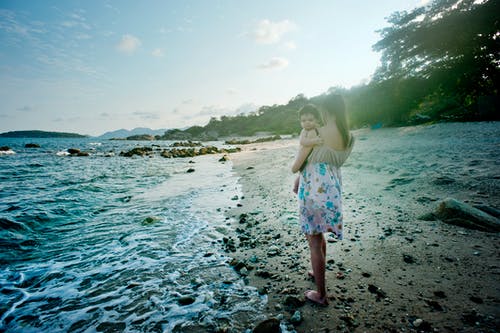 女人抱着婴儿在海边 · 免费素材图片