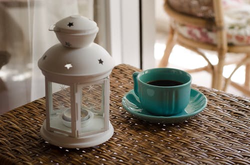 柳条桌上的蓝色陶瓷咖啡杯旁边的白色蜡烛灯笼 · 免费素材图片