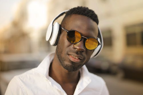 穿着黑色太阳镜和白色耳机的白衬衫的男人的选择性焦点特写照片 · 免费素材图片