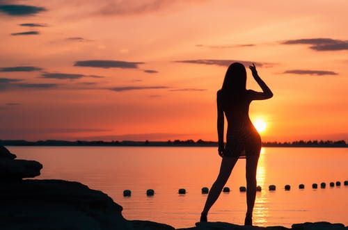 女人在日落时在水体附近的剪影 · 免费素材图片