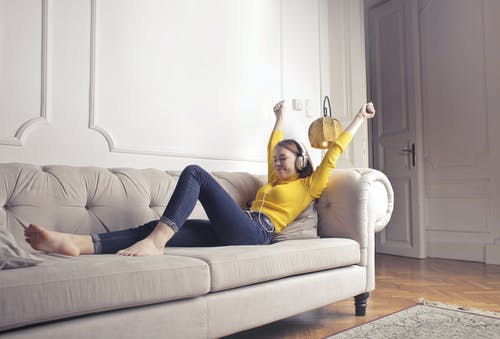 黄色长袖衬衫和蓝色牛仔牛仔裤，坐在白色的沙发上的女人 · 免费素材图片