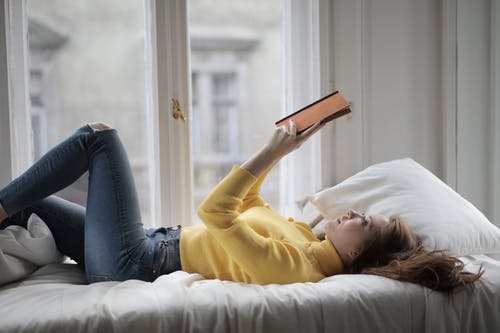 在看书时躺在床上的黄色毛衣的女人 · 免费素材图片
