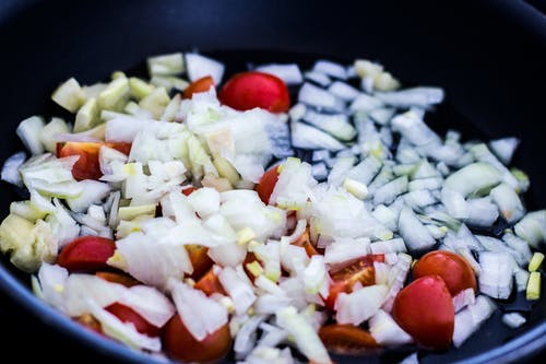 番茄和大蒜在黑色煎锅上煮熟 · 免费素材图片