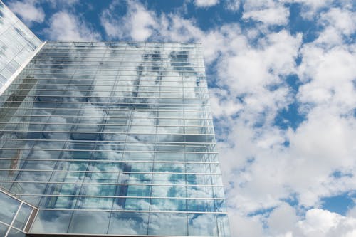 白天多云的天空下的透明玻璃建筑的底视图 · 免费素材图片