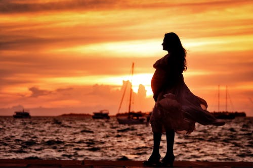 孕妇在日落时站在海边附近 · 免费素材图片