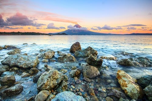 日落期间在海边的棕色和灰色岩石 · 免费素材图片