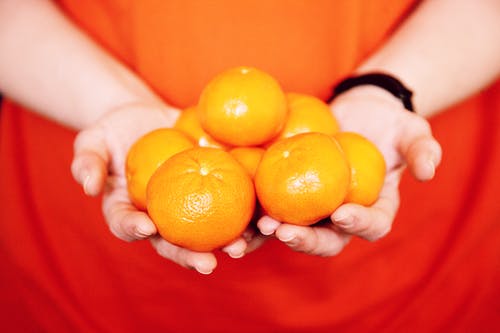 拿着橙色水果的人在关闭摄影 · 免费素材图片