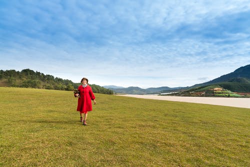 穿着红色绿色草坪上行走的女人的照片 · 免费素材图片