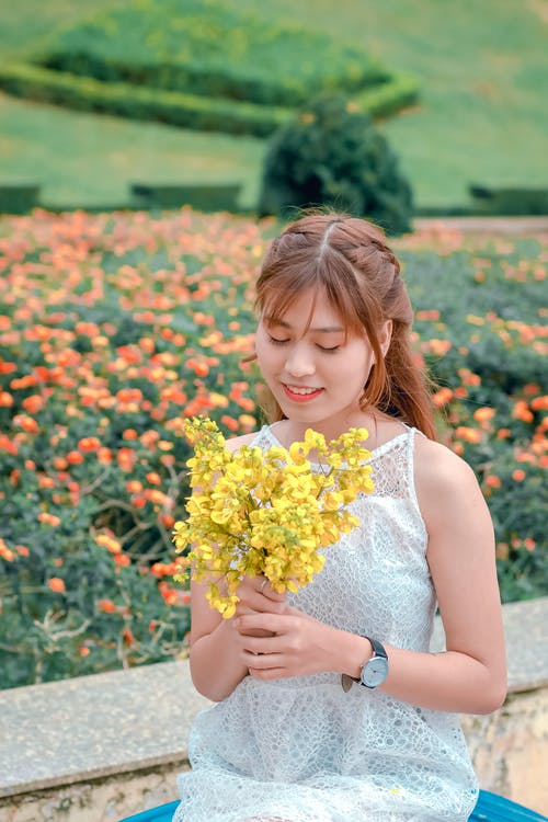 女人穿着白色上衣，拿着黄色的花瓣花 · 免费素材图片