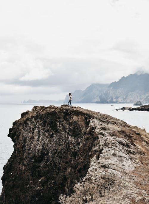 匿名的女性徒步旅行者在阴暗的日子享受从岩石峭壁顶部的海景 · 免费素材图片