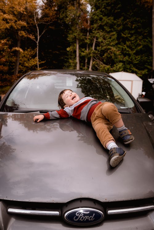 男孩躺在汽车引擎盖上的照片 · 免费素材图片