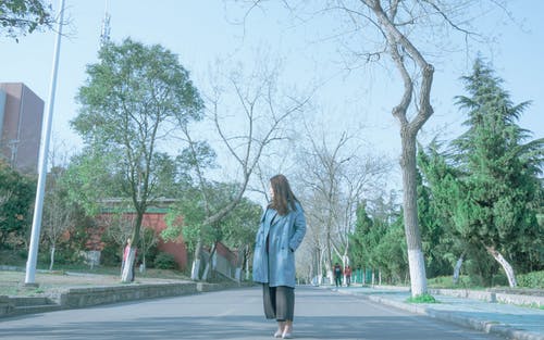 女人穿着蓝色外套站在沥青路面上 · 免费素材图片