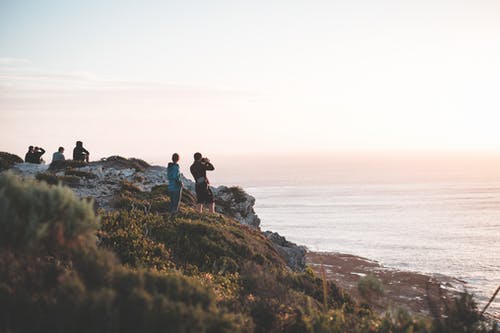 一群在日落时在多岩石的海滨上休息的旅行者 · 免费素材图片